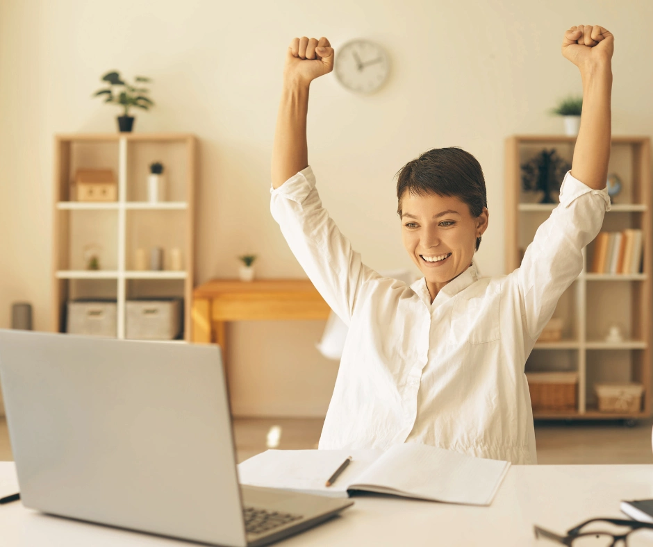 femme devant un ordinateur qui lève les bras au ciel car elle a réussi
