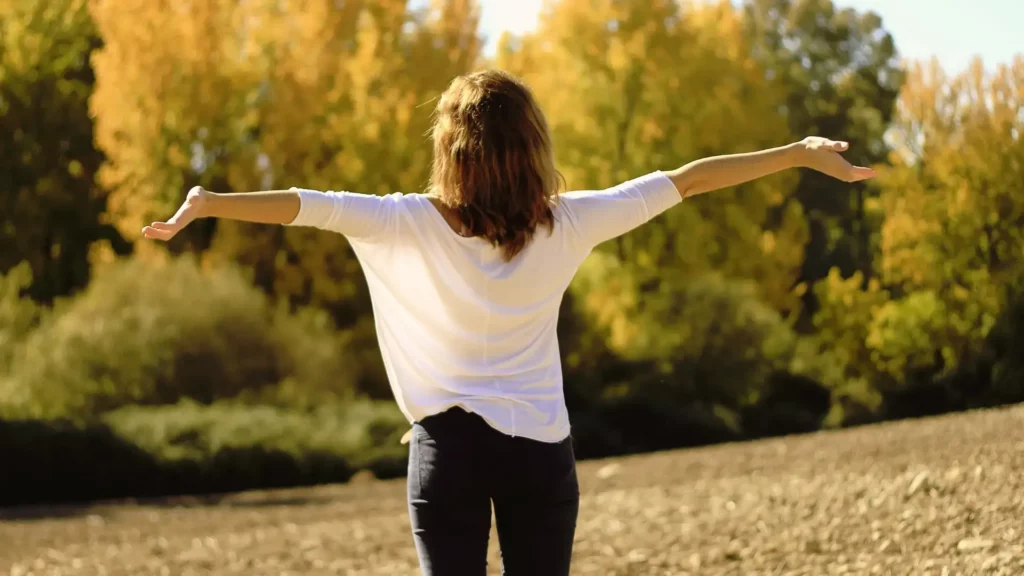 femme de dos dans la nature qui ouvre grand les bras avec confiance